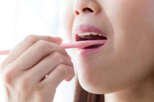ピンクの歯ブラシで歯を磨いてる女性