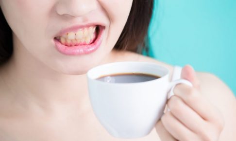 女性がコーヒーカップを片手に歯をむき出しにしている